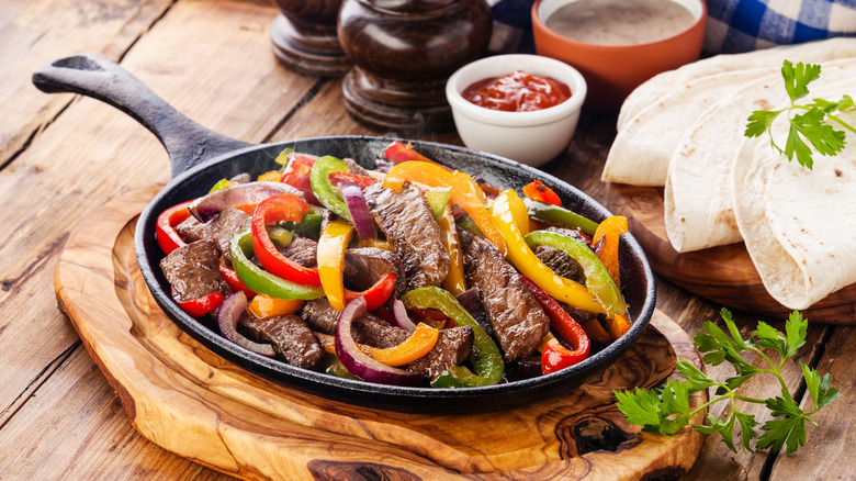 A sizzle platter of beef fajita fillings with peppers sittinng next to a platter of tortillas