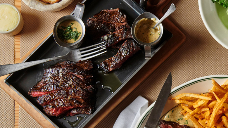 A tray of sliced, seared skirt steak served with ramakins of a cream colored sauce at Skirt Steak, NYC