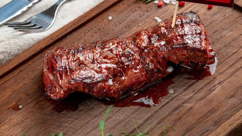 A skirt steak resting on a wooden cutting board.