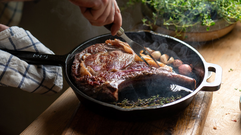 A big steak is seen cooking in a cast iron pan.