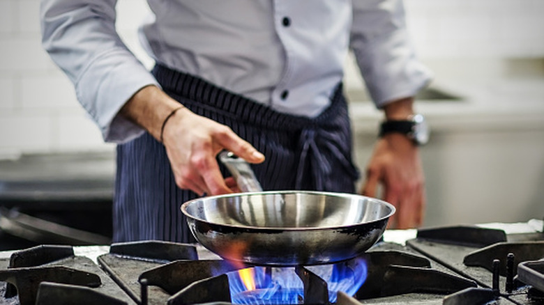 Person cooking with a stainless steel pan.