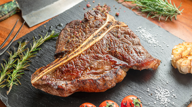 T-bone steak on a gray slate with tomatoes, salt, and herbs