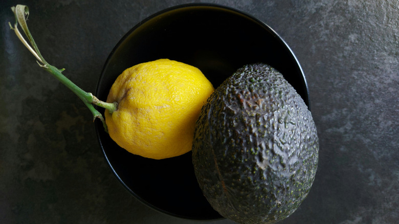 A lemon and an avocado in a black bowl