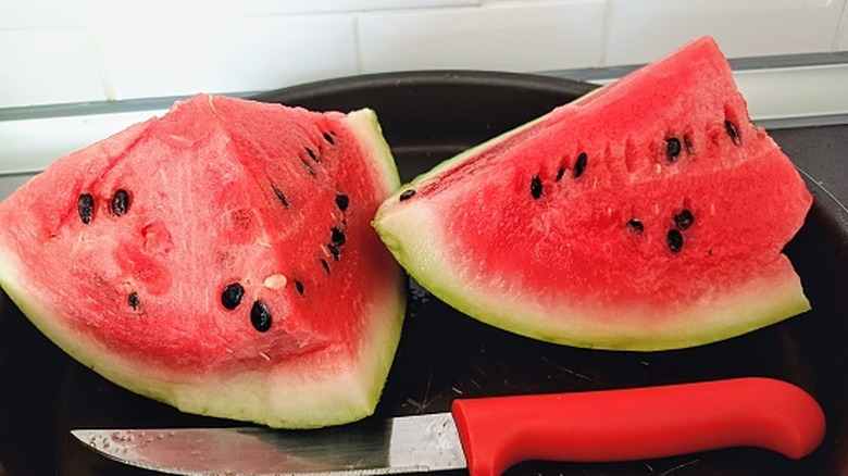 Cut watermelon on a black plate next to a knife