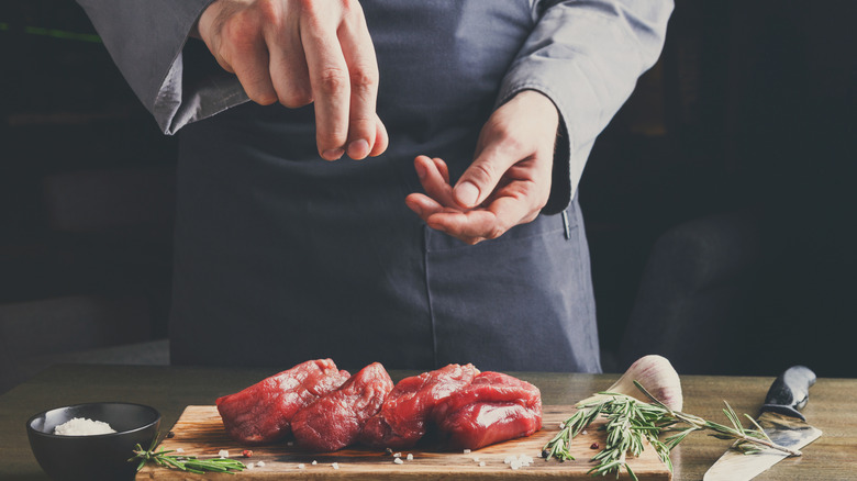 A man sprinkles salt on filet mignons