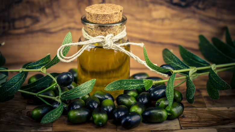 A small bottle of cold pressed olive oil with a cork sits on a wood background.