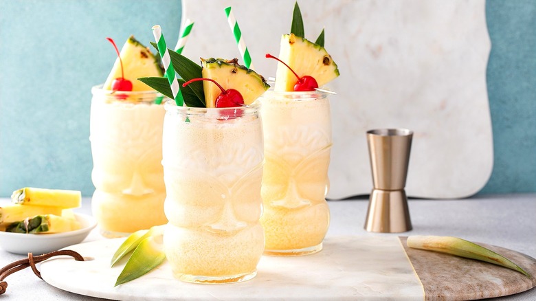 Three pineapple coconut cocktails in tiki glasses topped with wedges of fresh pineapple and maraschino cherries