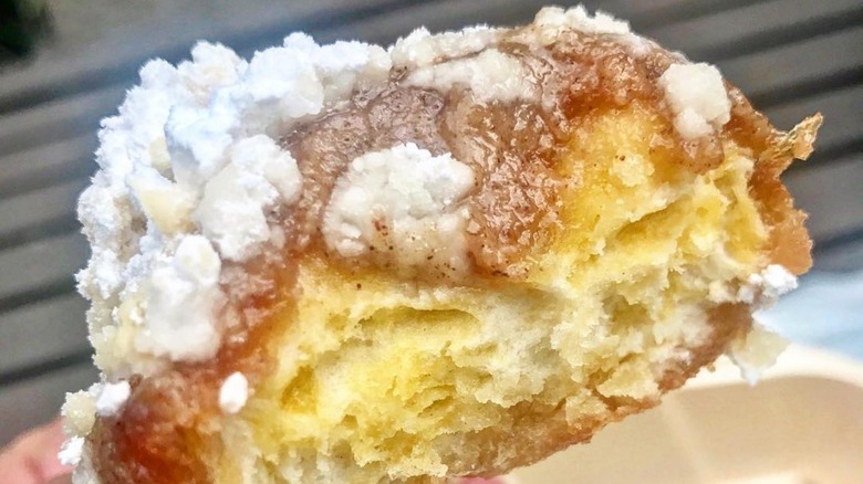 A close up of a half-bitten beignet with a creamy glaze and powdered sugar