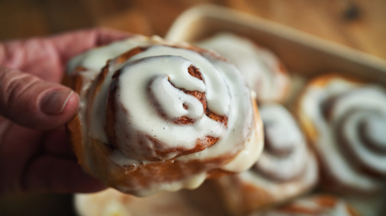 Close-up of a person holding a frosted cinnamon roll