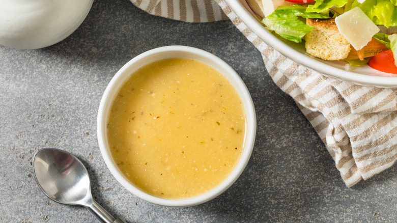 Top-down view of a white bowl of homemade Italian salad dressing next to a spoon and the edge of a salad bowl