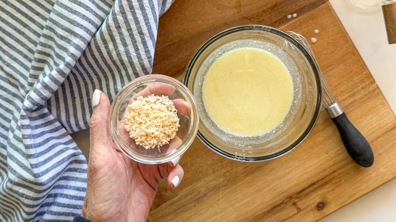 hand adding Parmesan to bowl