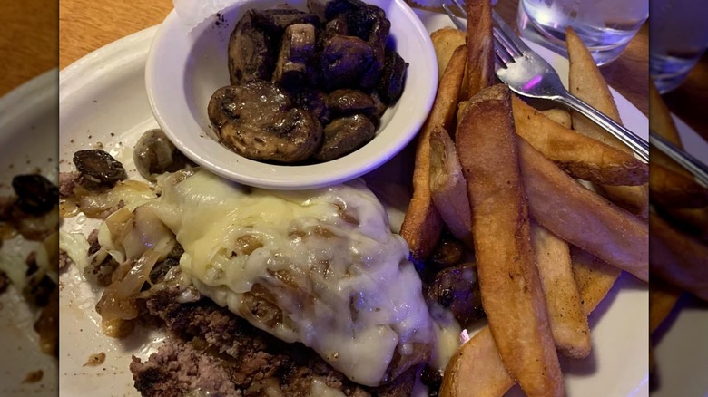 A picture of Texas Road House's Road Kill dish with steak fries and mushrooms on a plate