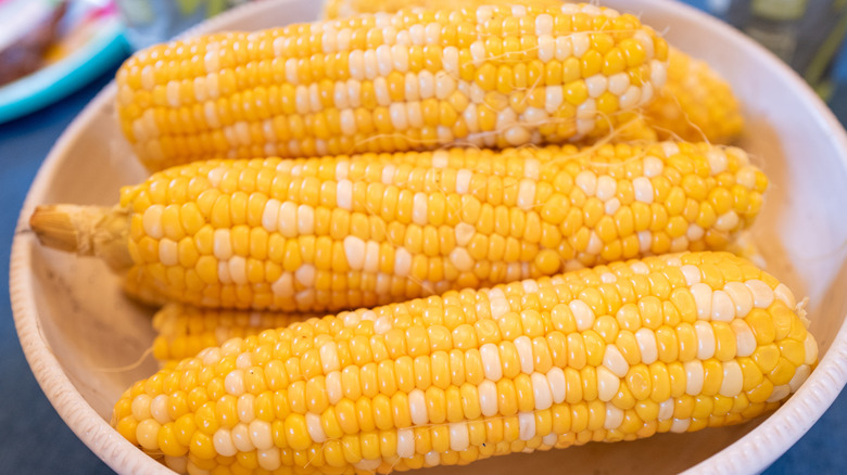 Ears of bright yellow corn on the cob are piled into a bowl.