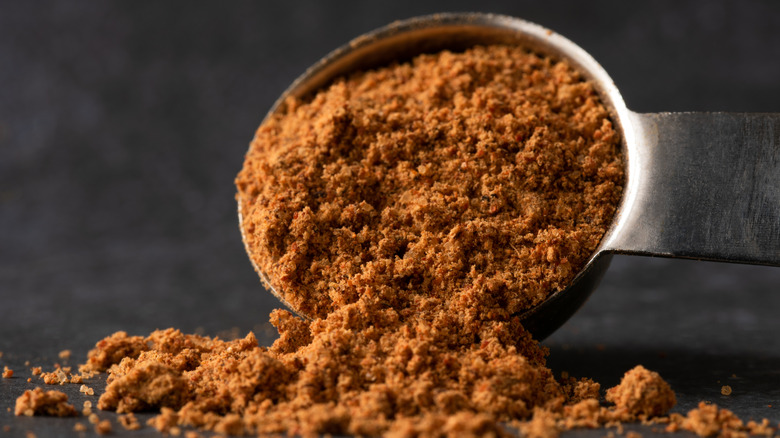 Taco seasoning spills out of a silver measuring spoon in close-up.