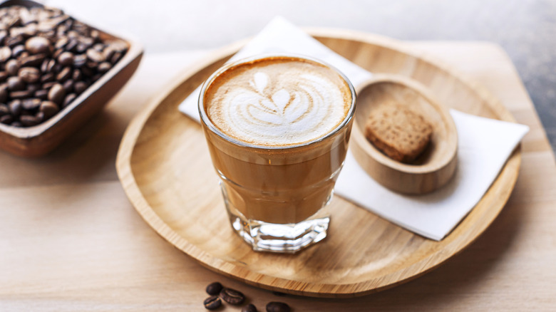 A cortado coffee on a tray next to a small cookie.