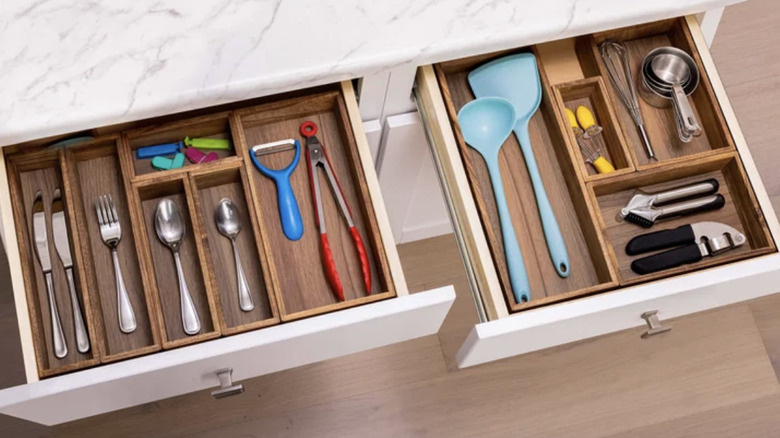 A very cluttered kitchen drawer with assorted tools, including scissors, a small juicer attachment, and other miscellaneous items.