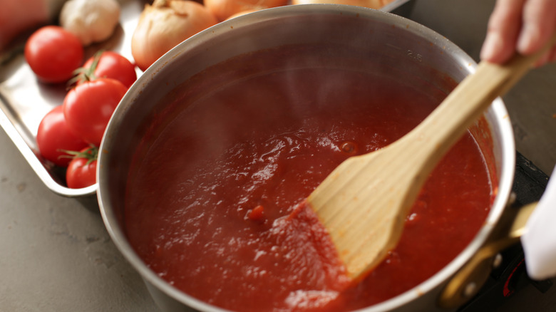 Person stirring tomato sauce in a stock pot with a wooden utensil