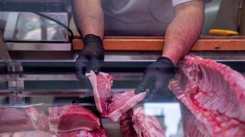 A butcher's hands are seen evaluating two cuts of steak.