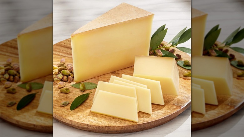 Comté cheese block next to smaller sliced piece on wood board with pistachios.