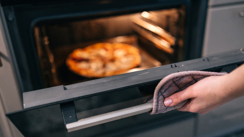 Person opening an oven door with a pie baking inside