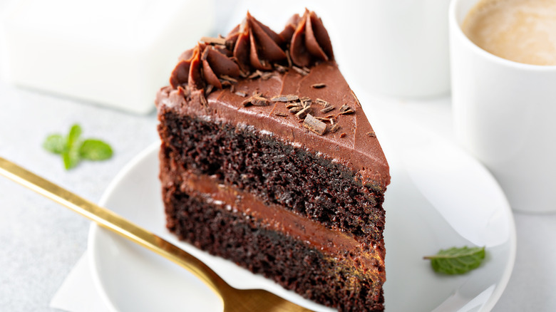 Slice of chocolate cake on a white plate with a fork.