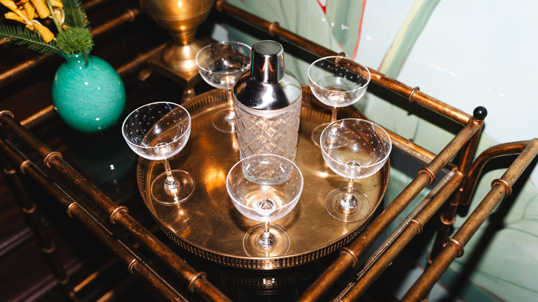 An attractive brass bar cart with a shaker and glasses is photographed from above