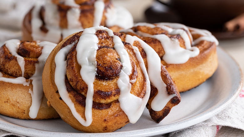 A closeup of a plate of cinnamon rolls with icing on them.