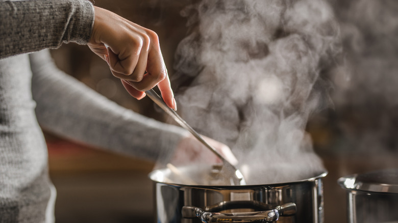 Close-up of a person stirring a steaming soup pot on the stove