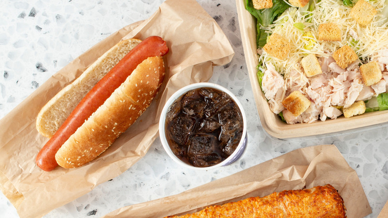 Top-down view of Costco hot dog and soda, chicken bake, and Caesar chicken salad