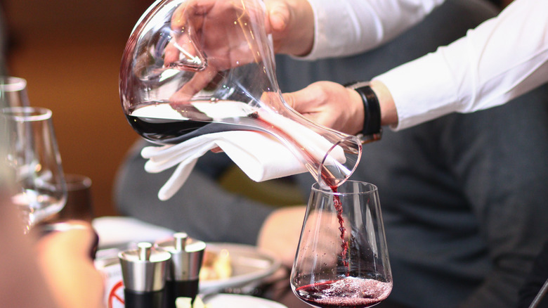 Waiter pouring wine from a decanter into a wine glass.