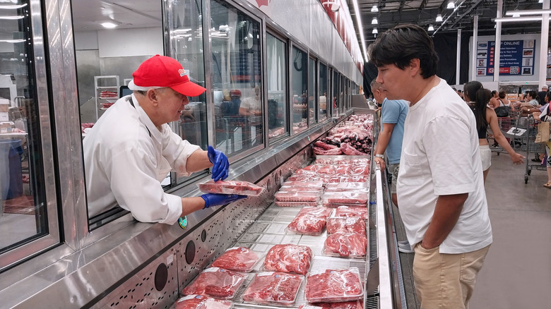 The meat aisle in Costco where an employee is helping a customer pick out meat