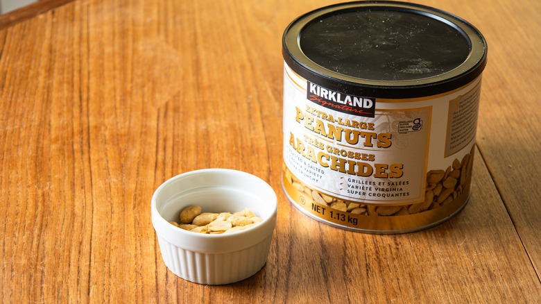 A container of Kirkland Super-Extra Large Peanuts beside a ramekin with nuts.