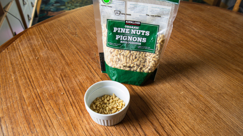 A bag of Kirkland Signature Organic Pine Nuts beside a ramekin with nuts.
