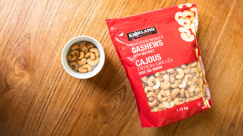 A bag of Kirkland Signature Roasted Whole Cashews with Salt beside a ramekin with nuts.