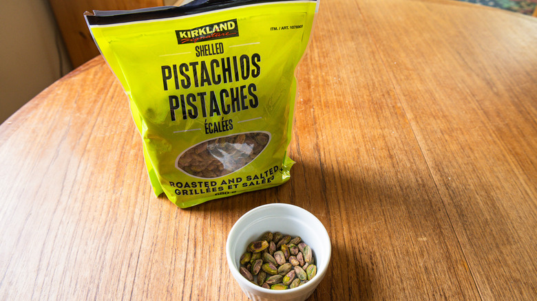 A bag of Kirkland Signature Pistachios beside a ramekin with nuts.