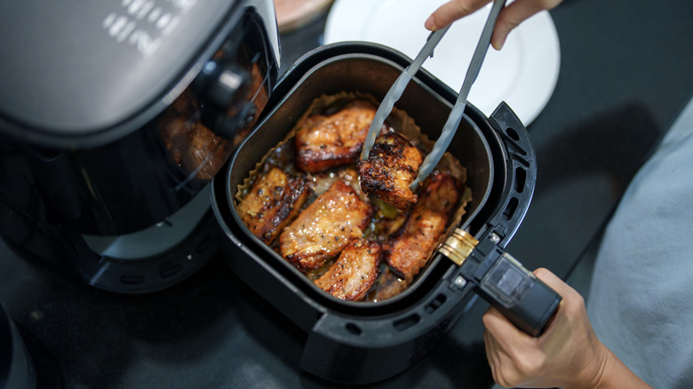 Tongs moving meat in an air fryer.