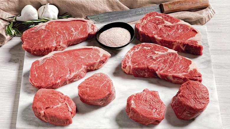 Eight raw cuts of steak from Rastelli on cutting board with small bowl of salt.