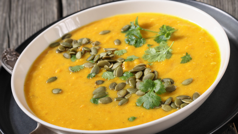 Pumpkin Red Lentil Soup topped with pumpkin seeds and cilantro in white bowl on rustic wooden table with spoon