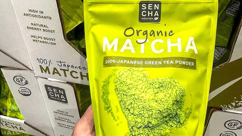 Hand holding 12-ounce bag of Sencha Naturals Organic Matcha Powder.