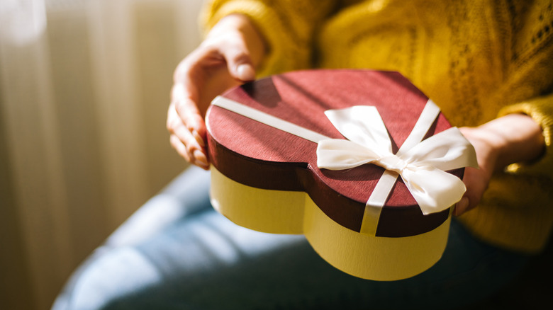 Person holding a heart-shaped gift box wrapped in ribbon