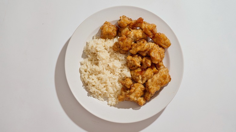 A plate of rice and orange chicken on a white table