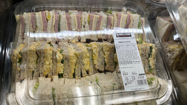 A Costco party platter made up of various sandwiches, in a plastic container.