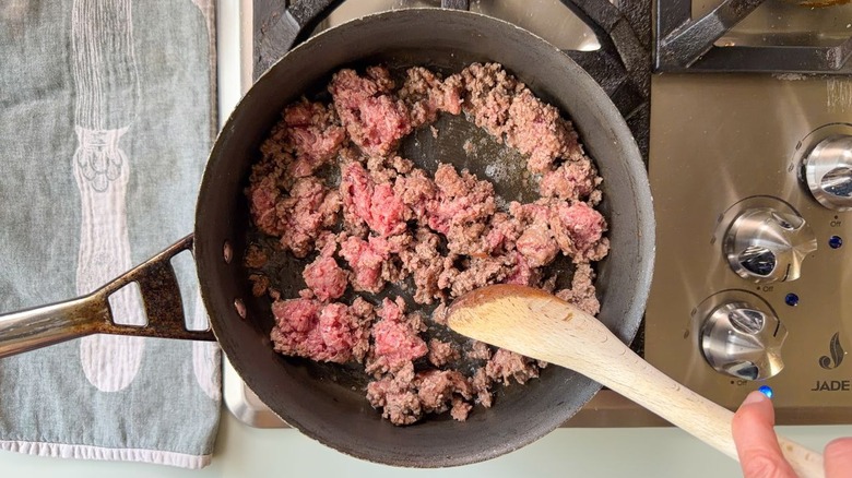 Browning ground beef in a skillet with a wooden spoon