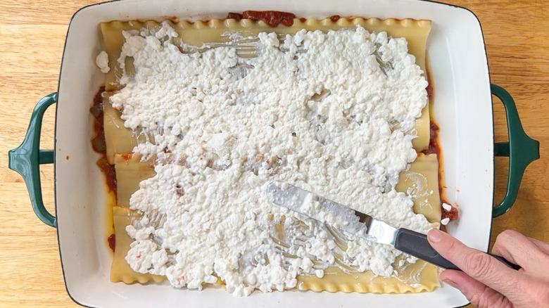 Spreading a layer of cottage cheese over lasagna noodles using an offset spatula in a 13 x 9-inch pan