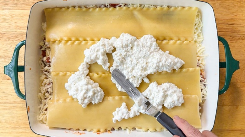 Spreading cottage cheese on lasagna noodles with offset spatula in 13 x 9-inch pan