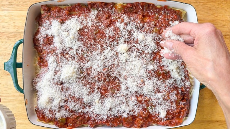 Sprinkling grated Parmesan cheese over unbaked cottage cheese lasagna in 13 x 9-inch pan