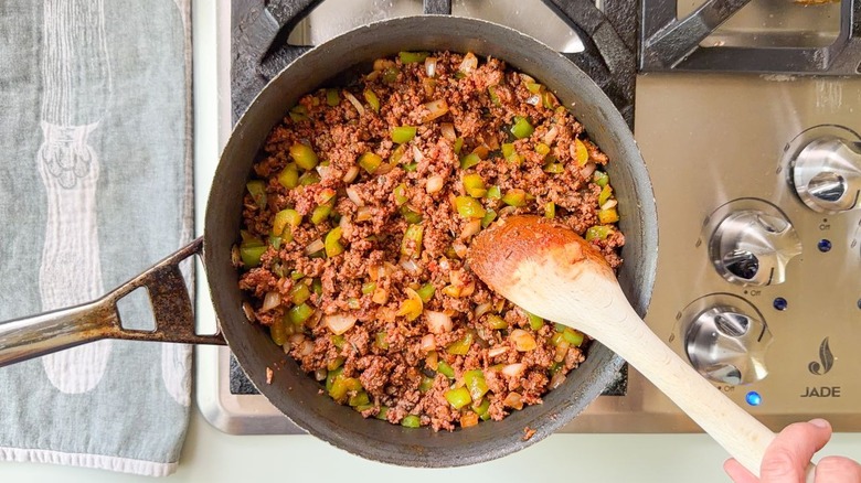Stirring ground beef and tomato paste in skillet with wooden spoon