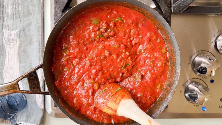 Stirring tomato sauce and basil into ground beef and vegetables