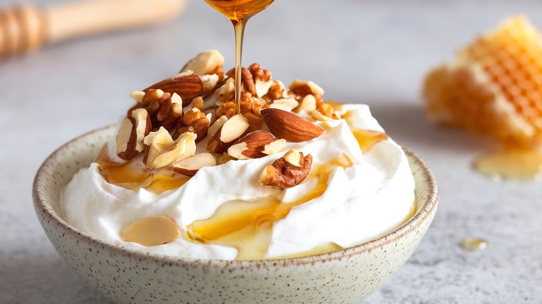 Honey being poured on a bowl of Greek yogurt with almonds and walnuts
