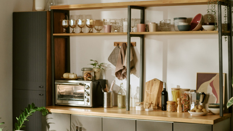 A toaster oven and dishware are stored on a baker's rack
